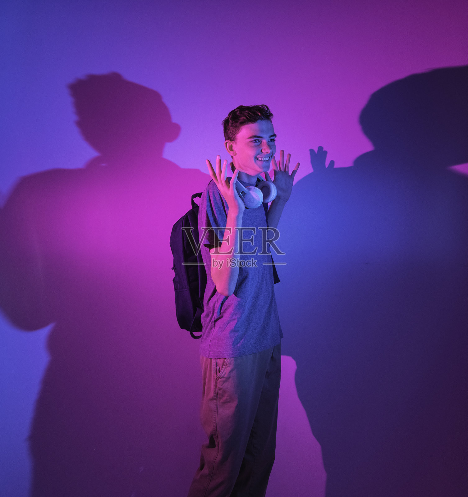 彩色背景前戴着耳机、拿着包的白人高中男生照片摄影图片