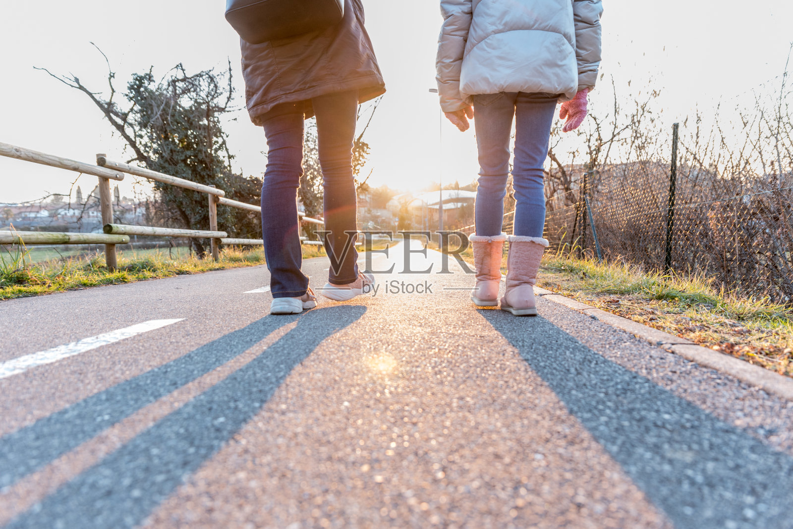 晴朗冬日下午,母亲和女儿在城市人行道上一起行走的后视图照片摄影图片