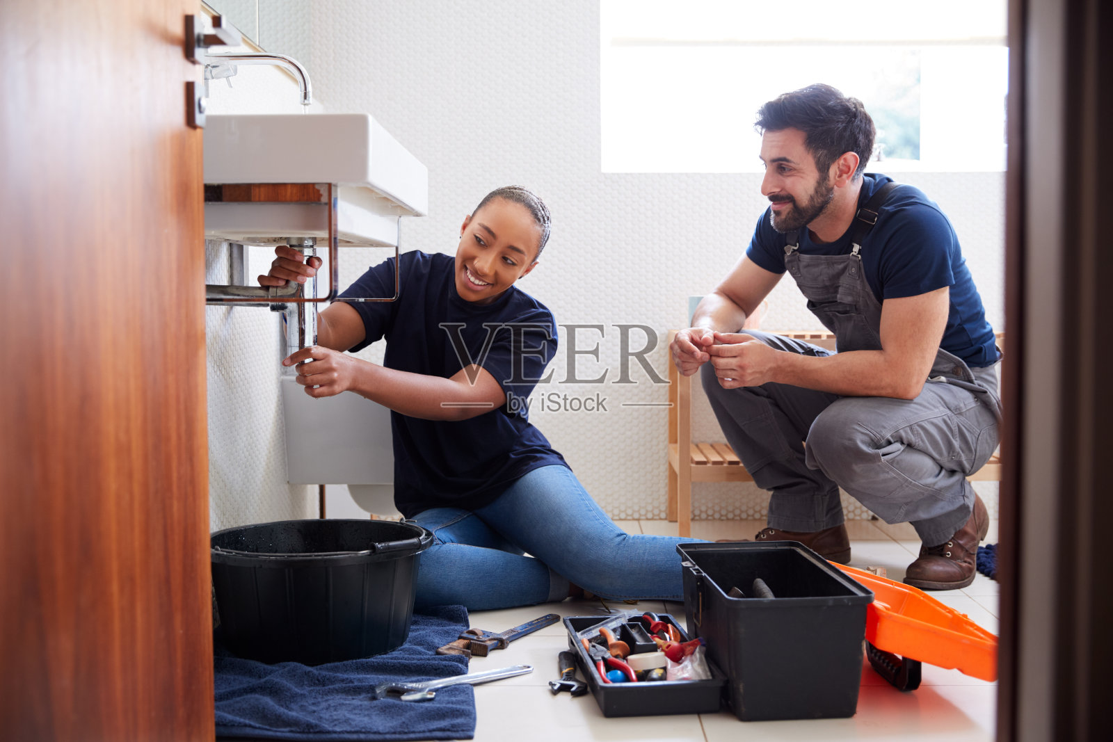 男水管工教女学徒修理家用浴室中漏水的水槽照片摄影图片