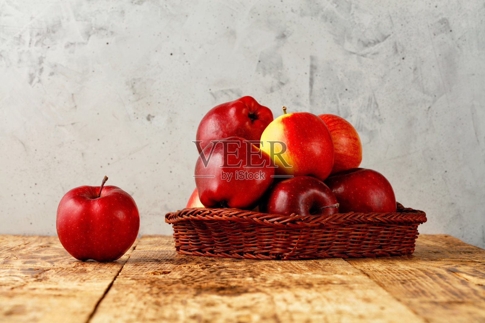 成熟的红苹果躺在一个柳条篮子里,放在一张旧木桌上,背景是灰色的混凝土。照片摄影图片