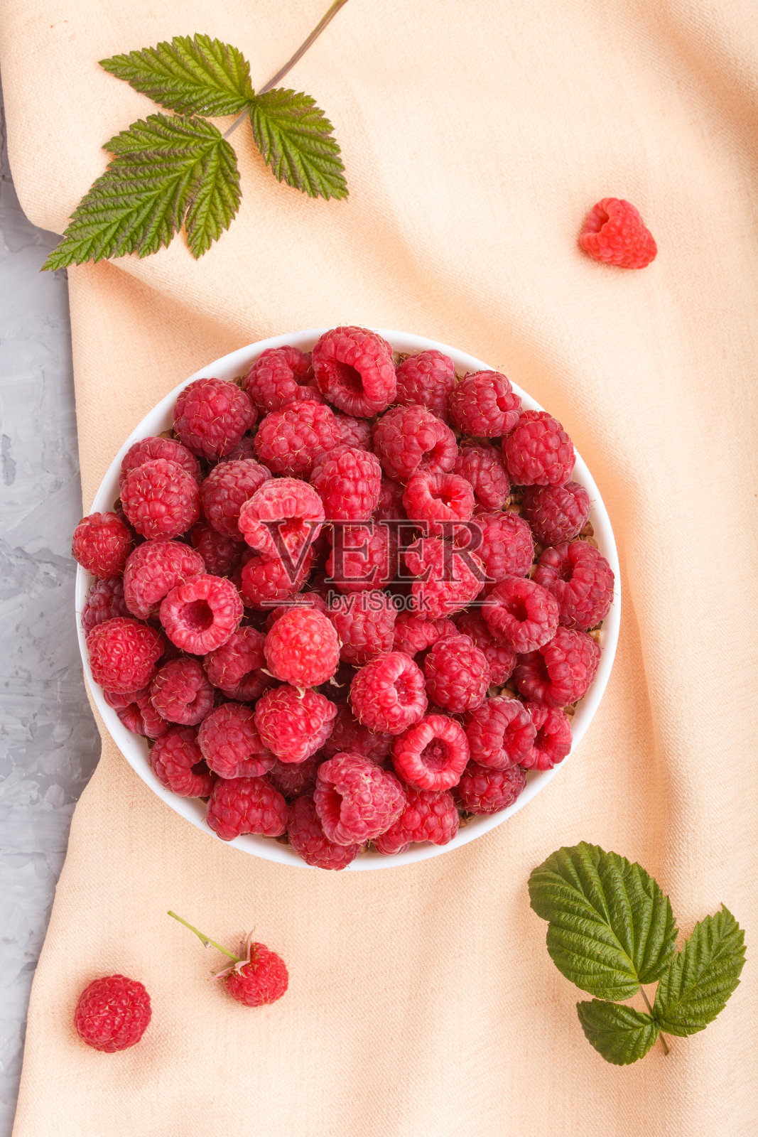 新鲜的覆盆子在白色的碗和橙色柔和的纺织品在灰色的混凝土背景。俯视图,平躺,特写。照片摄影图片