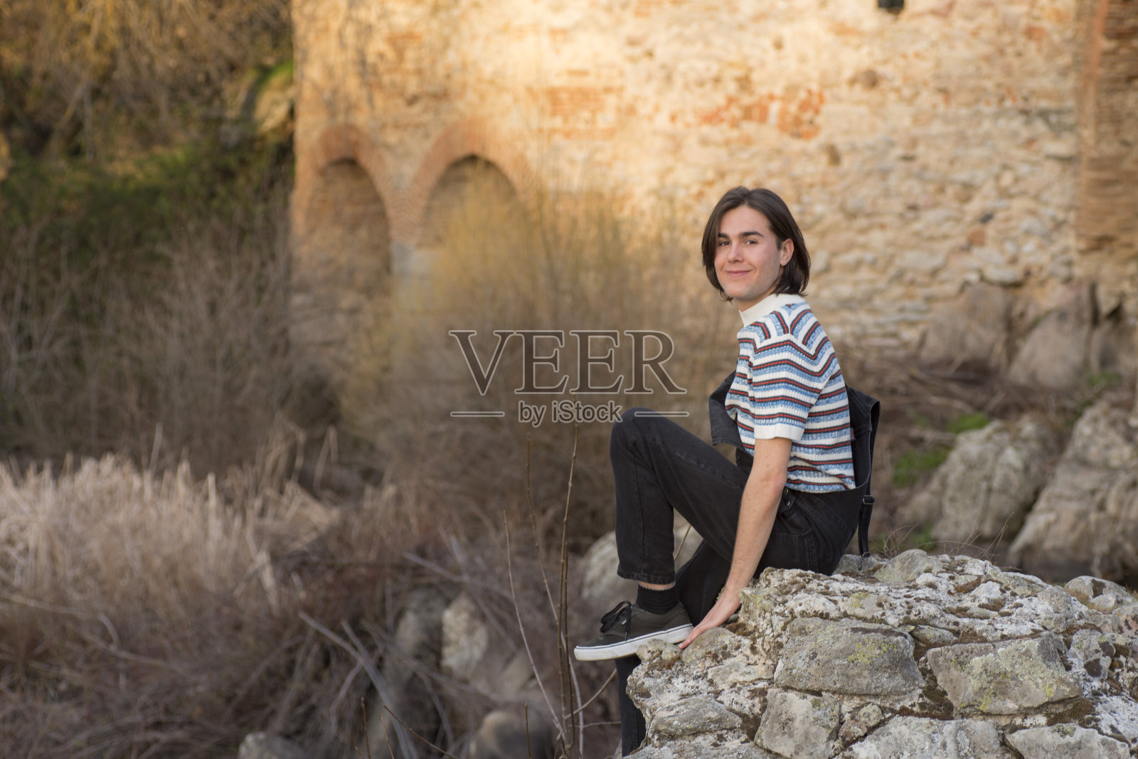 在田野和桥梁背景前摆姿势的年轻男子照片摄影图片