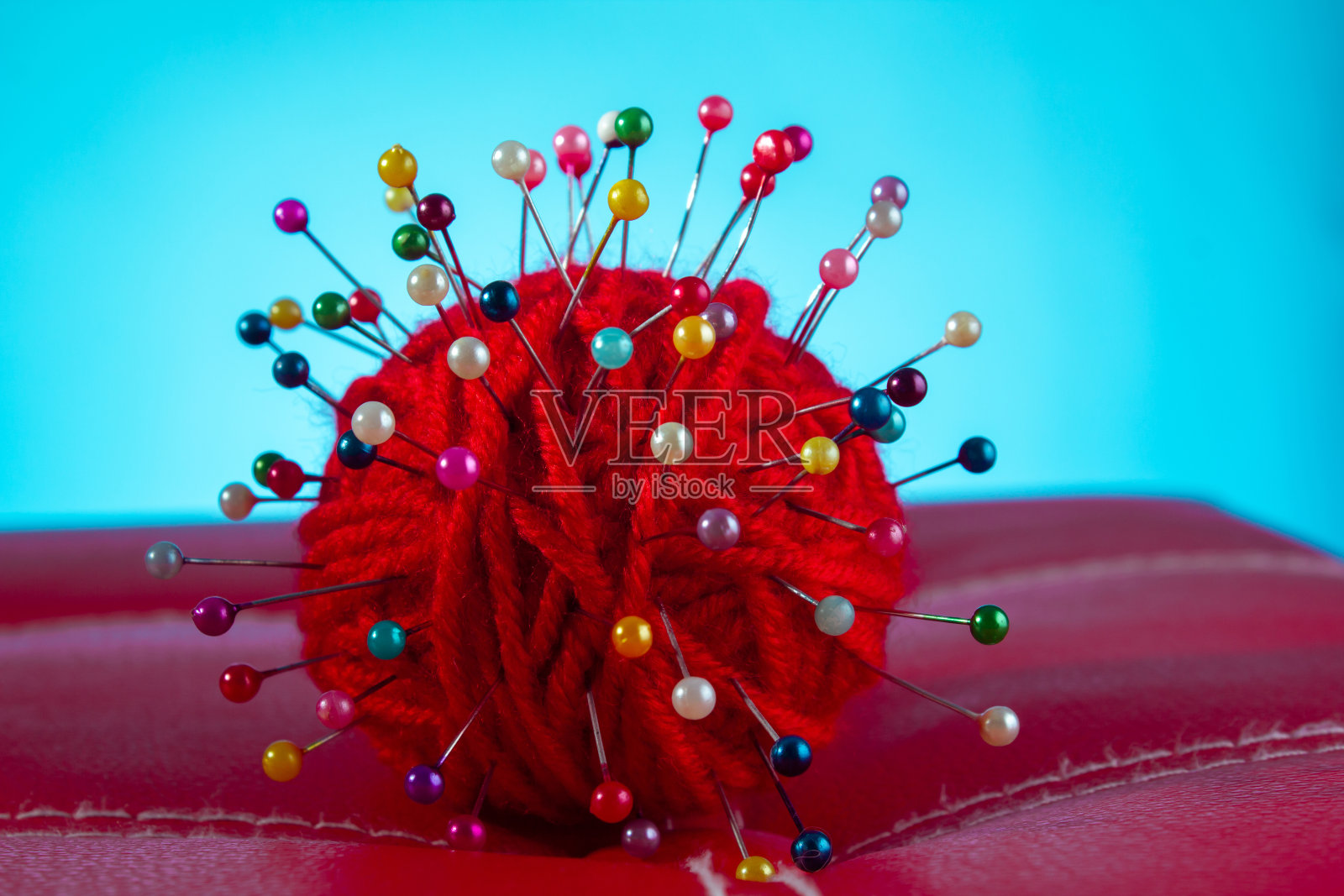 一根红线在蓝色背景的红皮革上扎了很多针。关闭拷贝空间照片摄影图片