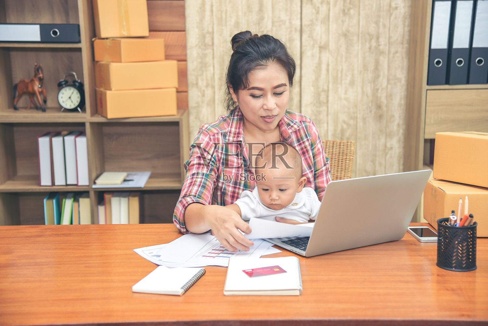 年轻漂亮的单身妈妈在家用笔记本电脑工作,同时抱着女儿坐在她的腿上,看着妈妈工作照片摄影图片