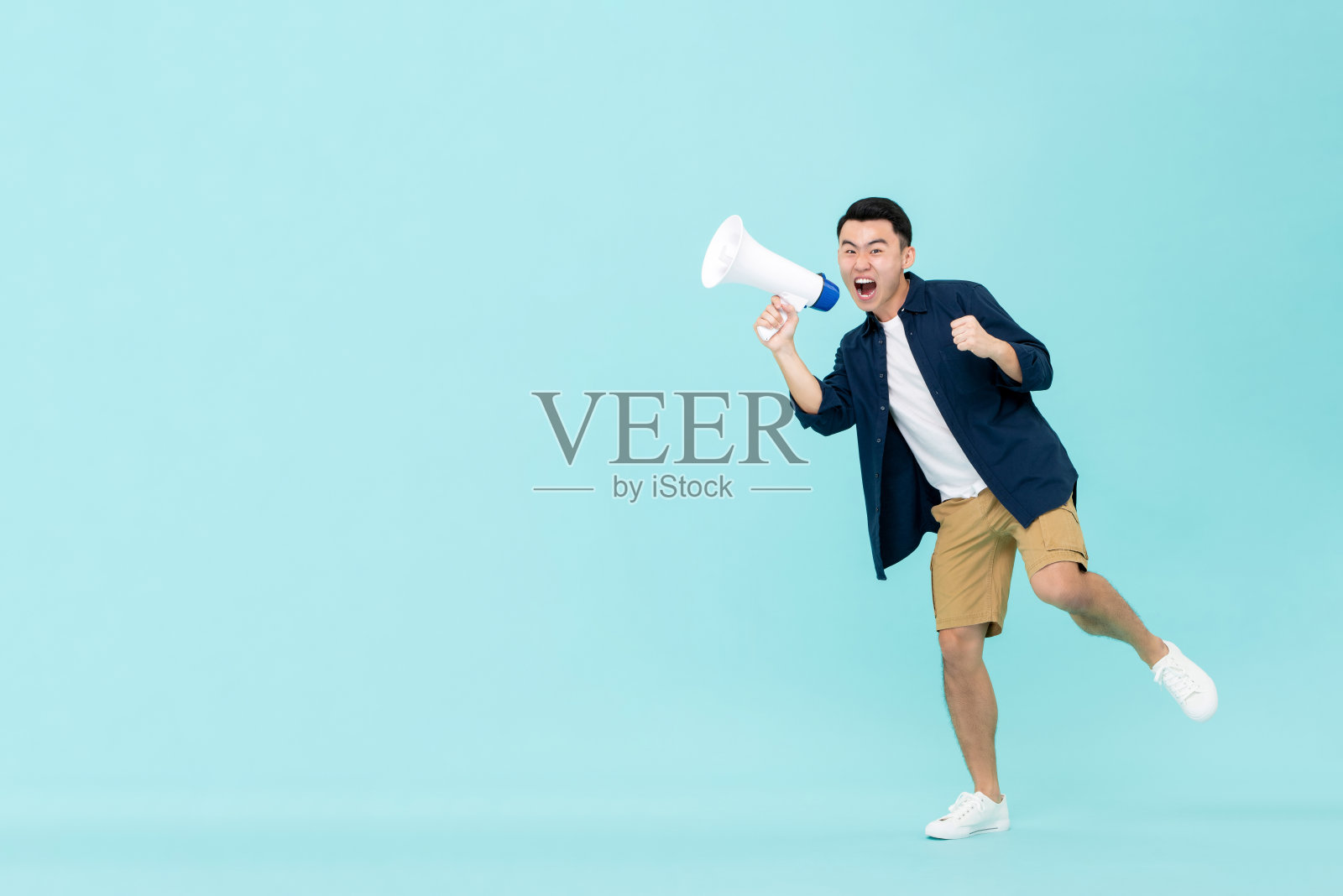 兴奋的年轻亚洲男人拿着扩音器大喊。照片摄影图片