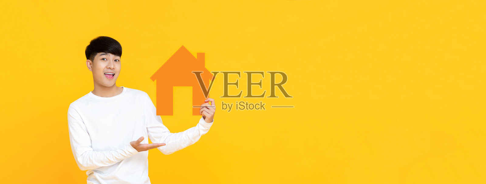 微笑英俊的亚洲男人在旗帜黄色的背景上举着房子标志照片摄影图片