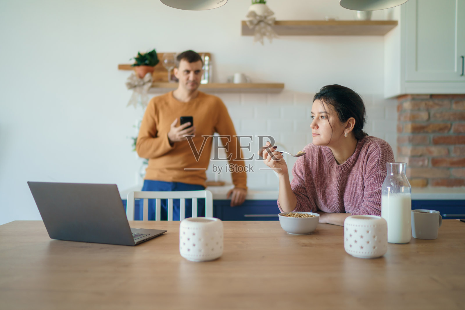 年轻夫妇在家中厨房一边享用早餐,一边使用笔记本电脑或阅读新闻,共同规划假期照片摄影图片