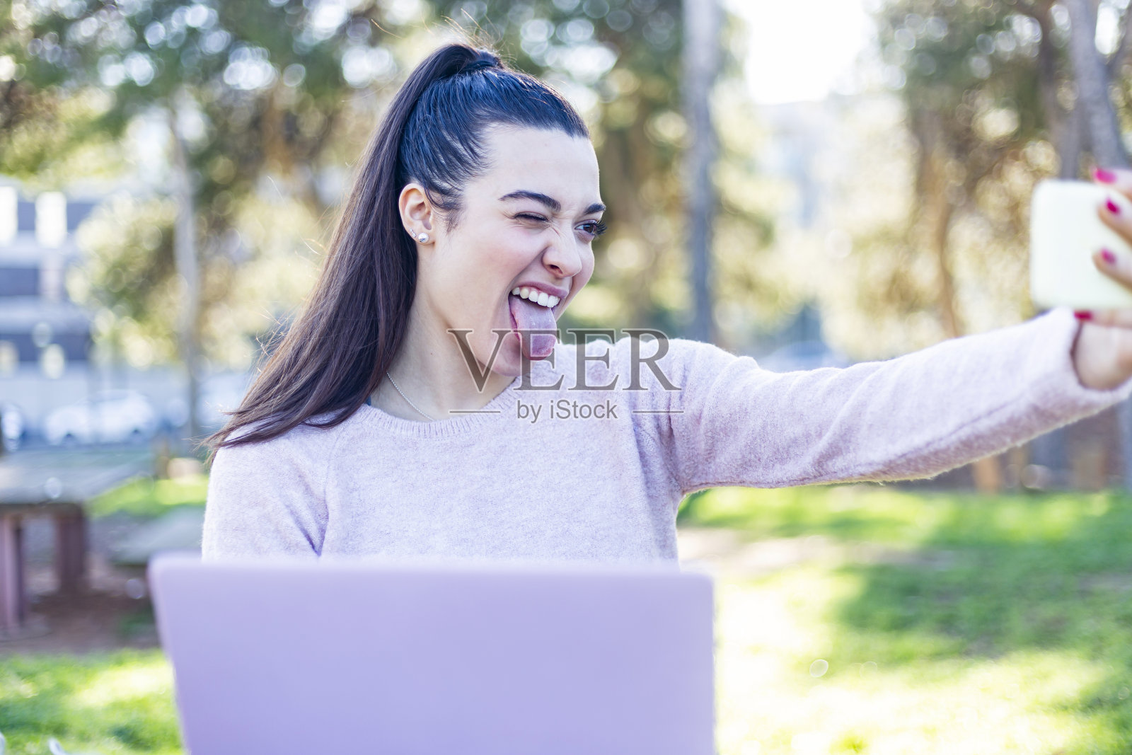 一位美丽的年轻女子,扎着马尾辫,坐在公园里,做着手势自拍照片摄影图片