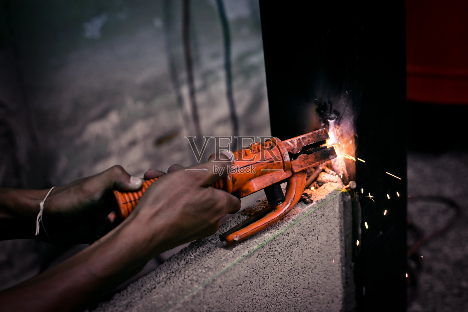 工作中焊接铁件的工业工人。在制造业进行手工铁焊的男人。照片摄影图片