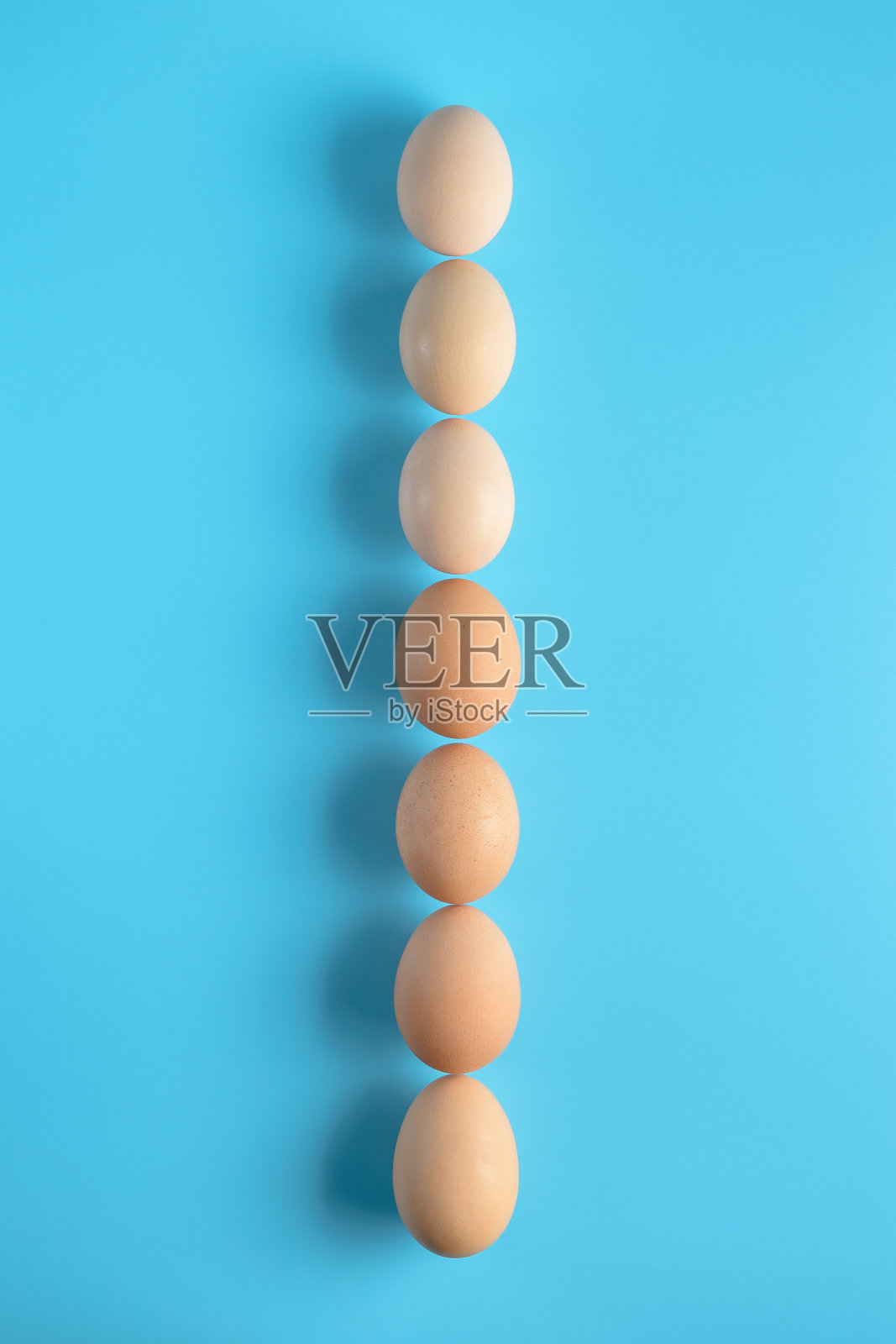 七个新鲜的棕色鸡蛋排在蓝色的背景上。健康的营养。天然有机农产品。照片摄影图片