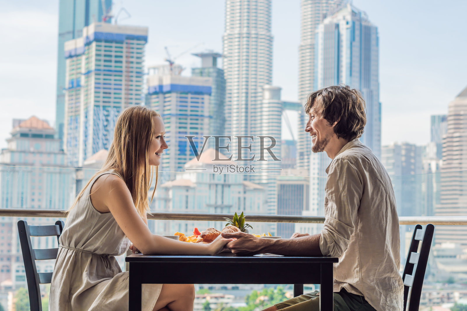 情侣在阳台上享用早餐,背景是大城市照片摄影图片