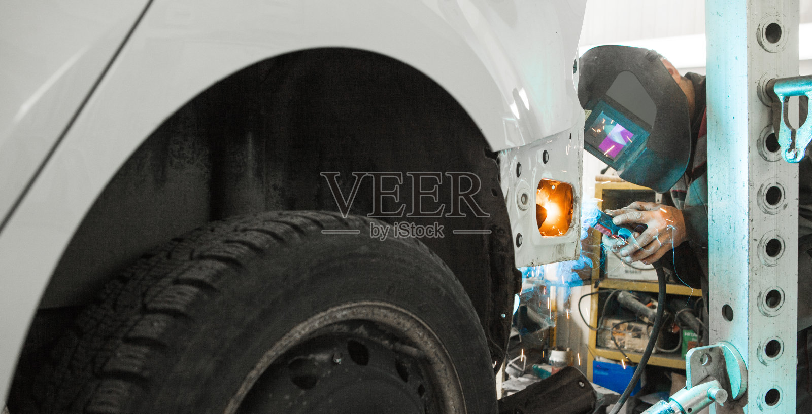 戴防护面罩的年轻男人在车库修理旧车身,焊接车辆照片摄影图片