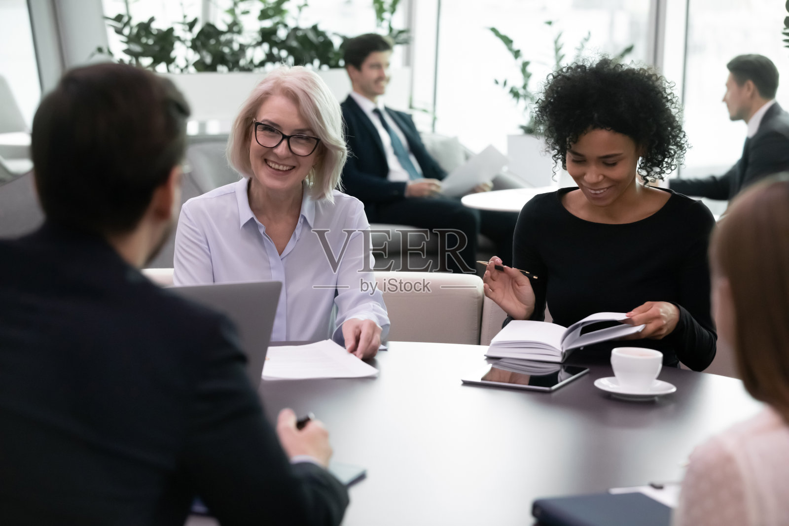 在现代办公室里开会的微笑的不同年龄的多种族商务人士照片摄影图片