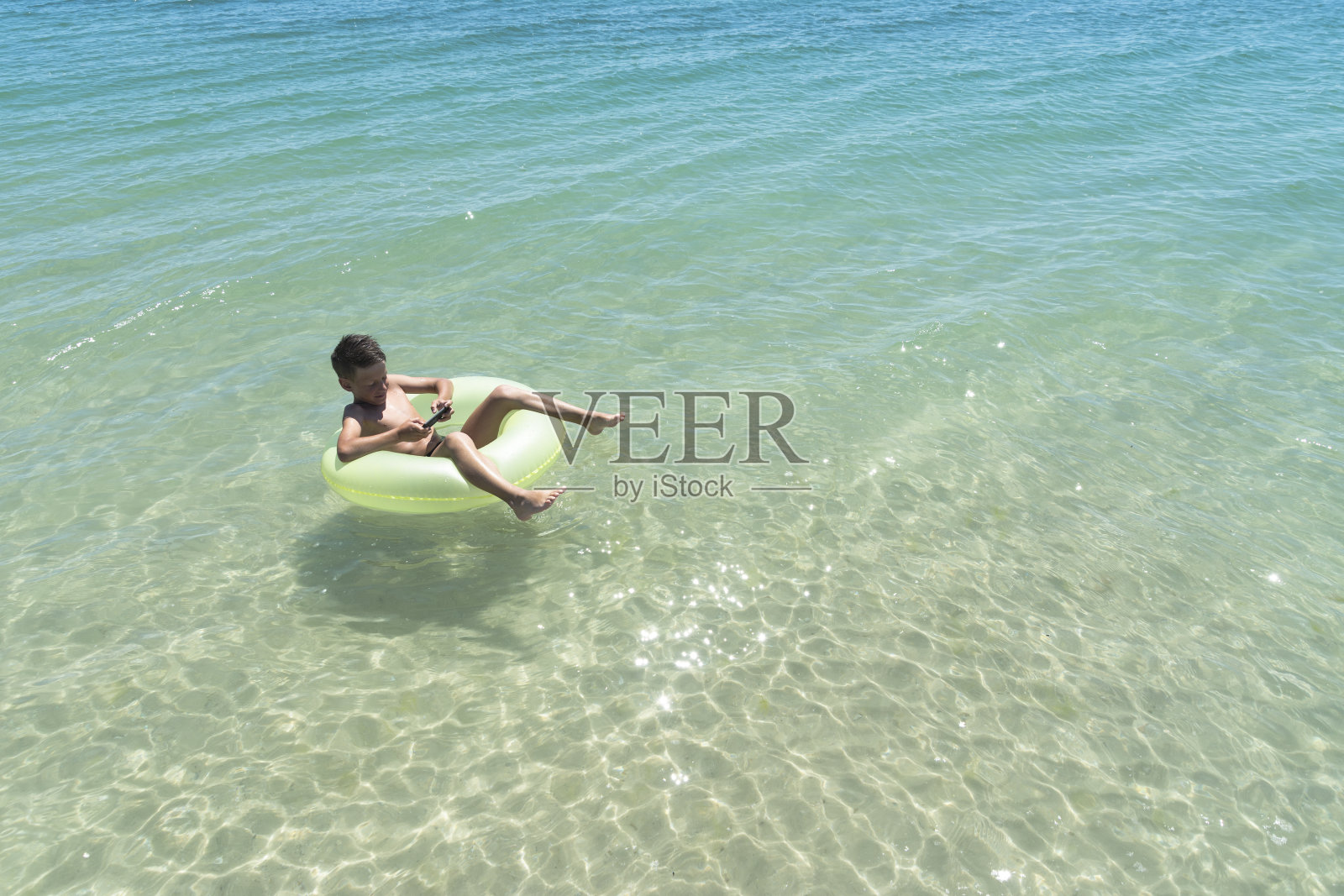 带着智能手机的男孩漂在海里照片摄影图片