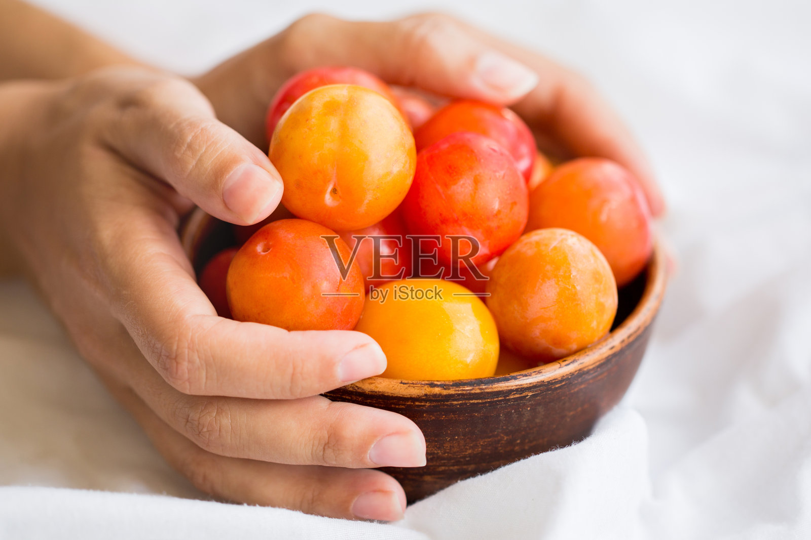 熟透的黄梅放在一个陶碗里,手里拿着白布。照片摄影图片