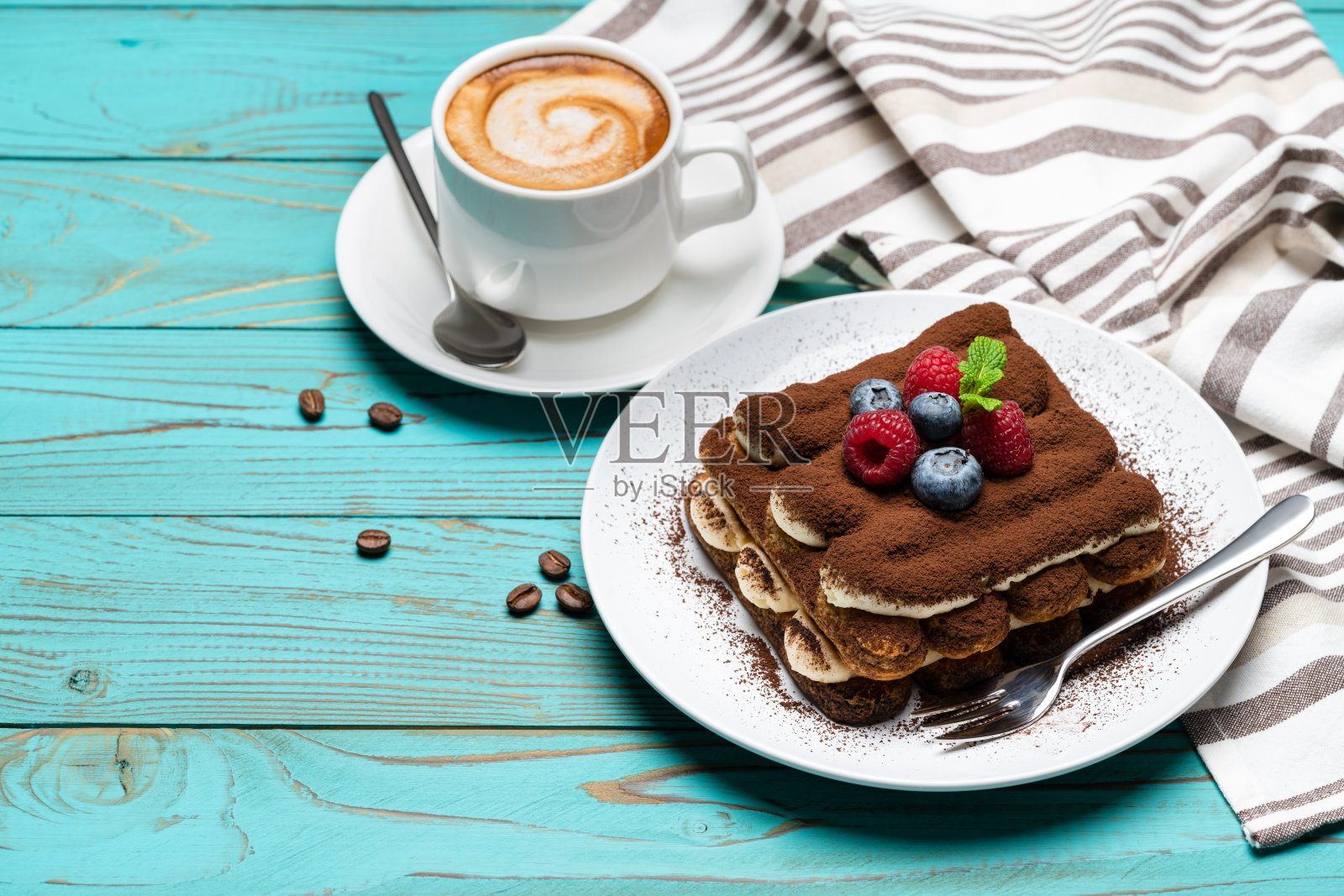 一份经典的提拉米苏甜点,配上树莓和蓝莓,再配上一杯在蓝色木质背景上的浓咖啡照片摄影图片