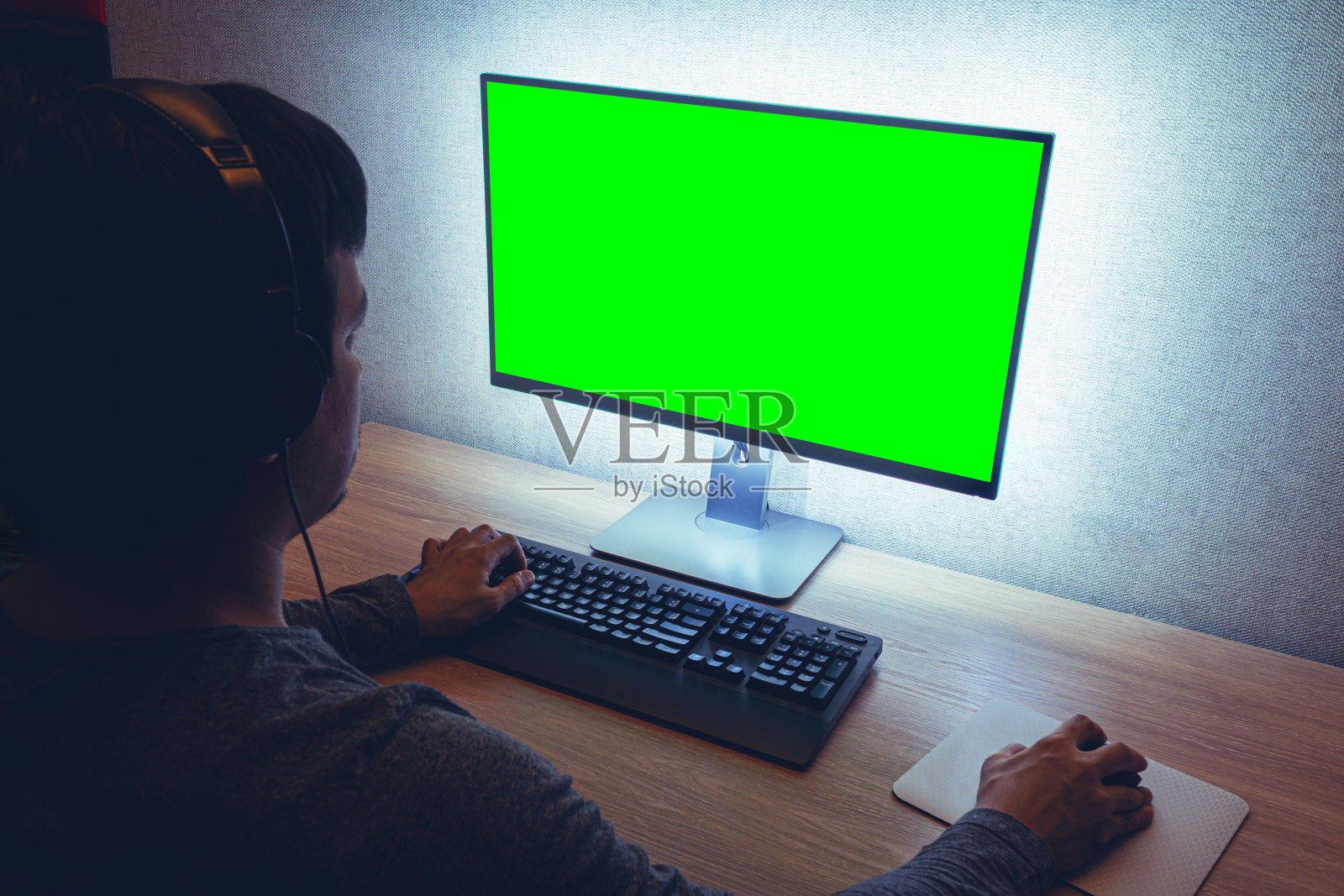 戴耳机男子坐在黑暗房间的显示器前照片摄影图片