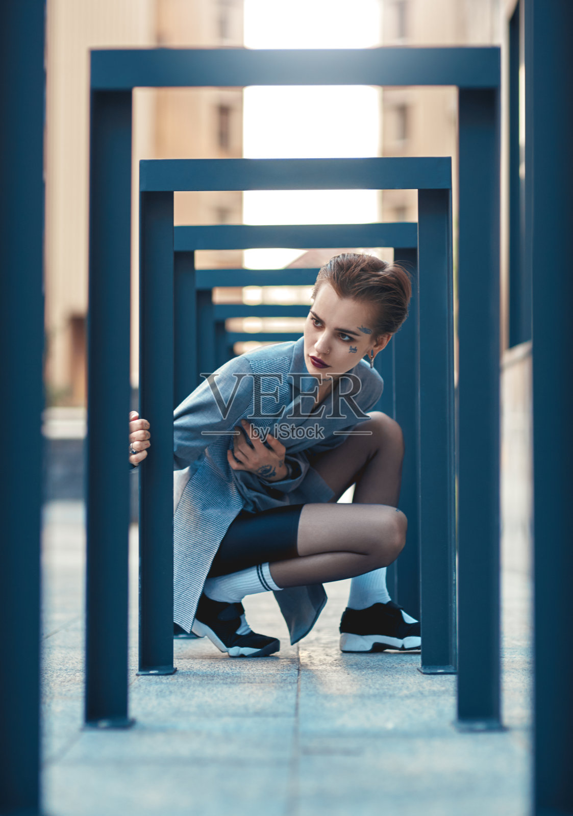 潮流都市风:身穿外套的年轻时尚女性坐在户外,好奇地触摸着栅栏照片摄影图片