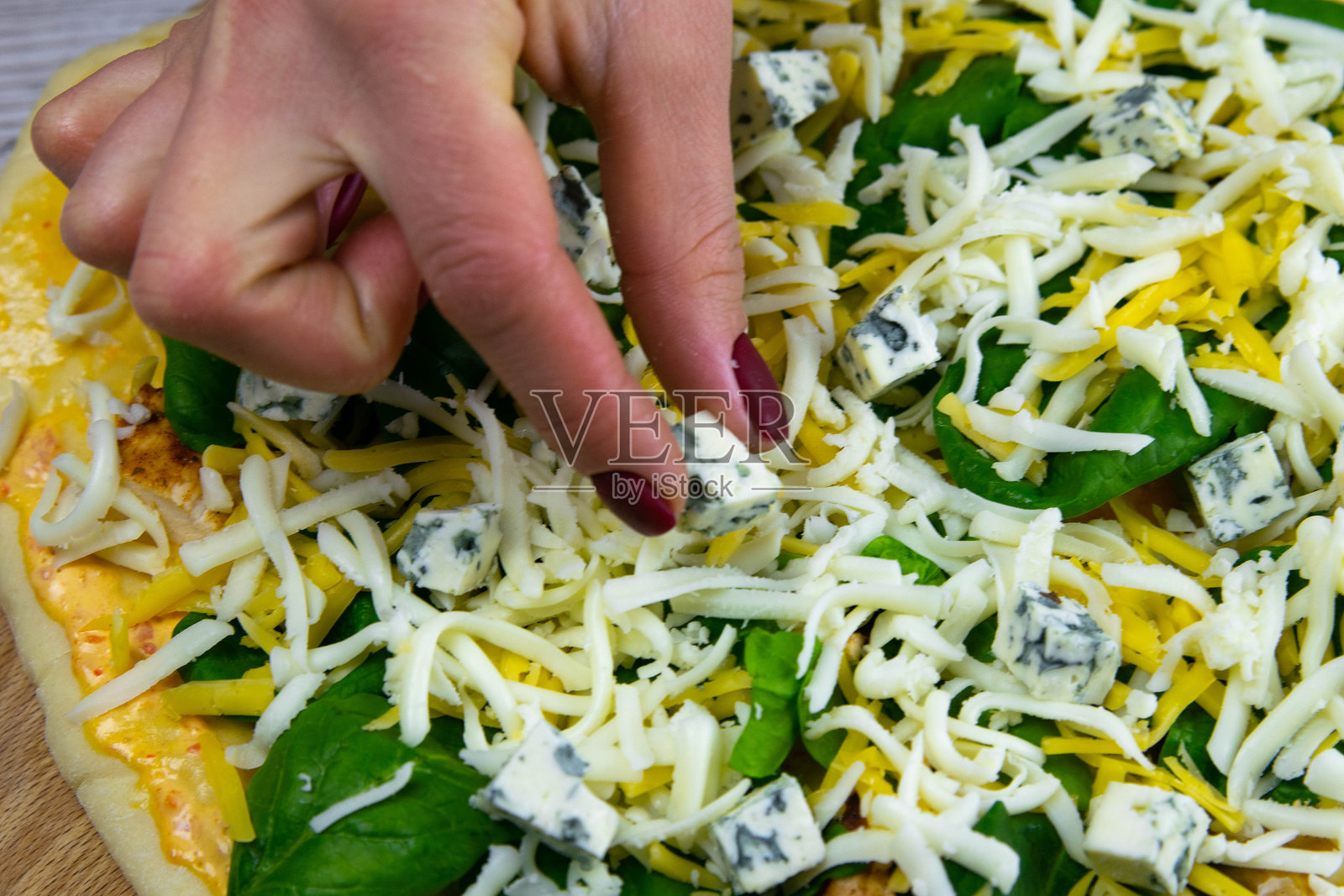 女人手在披萨上放奶酪块,新鲜的意大利原味生披萨准备过程照片摄影图片