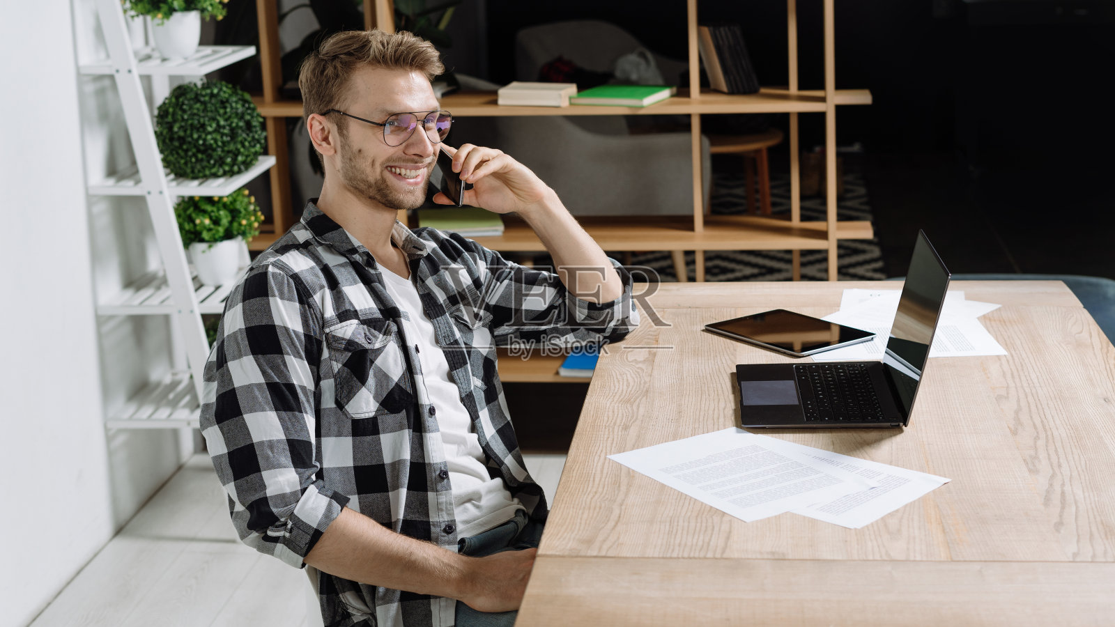 年轻的自由职业者坐在办公室里用笔记本电脑和智能手机聊天照片摄影图片