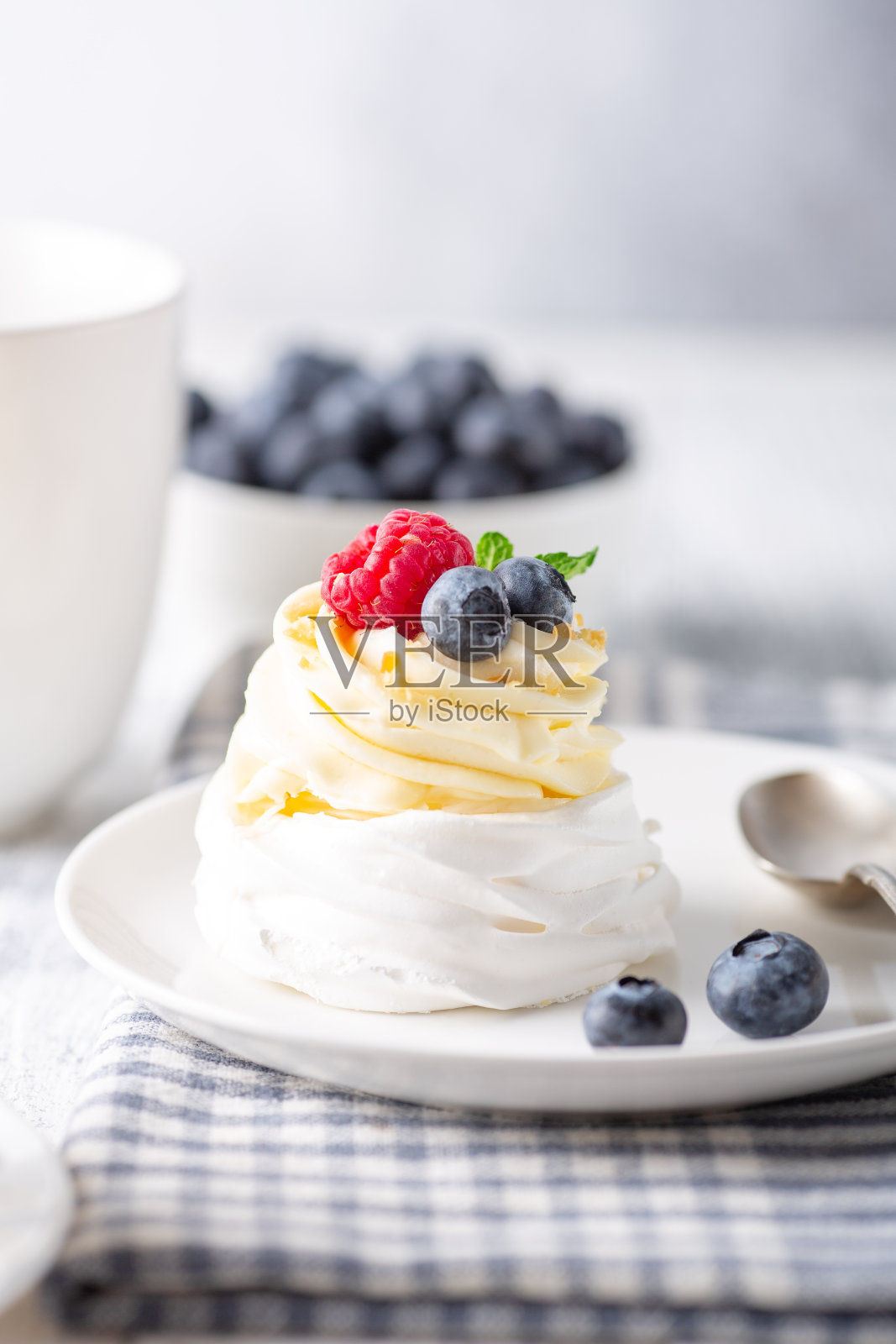 咖啡杯,奶油巴芙洛娃蛋糕,白盘子上有新鲜浆果。北欧风格。软焦点照片摄影图片
