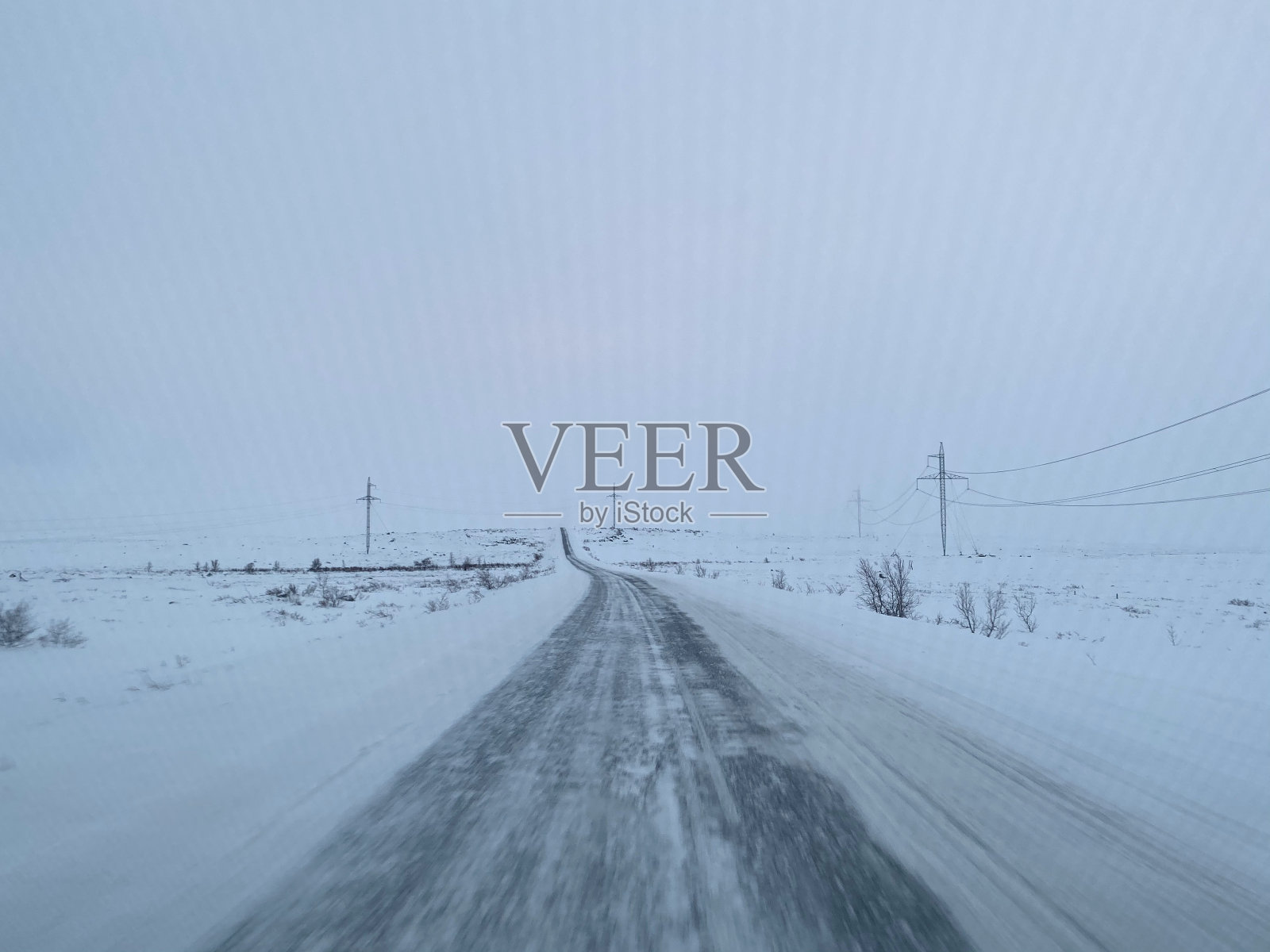 冬季多云的天气,路边的积雪和干草覆盖着空旷的道路。照片摄影图片