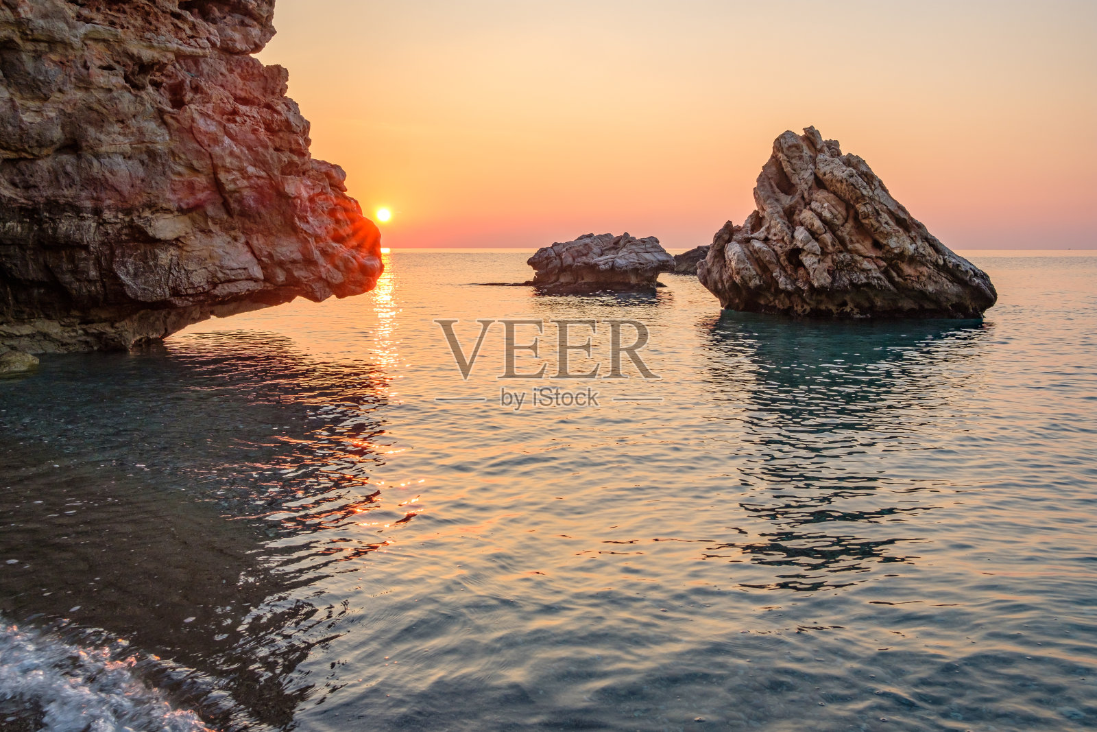 黎明时分,布满岩石的海岸,太阳越过海面,小路倒映在水面上照片摄影图片