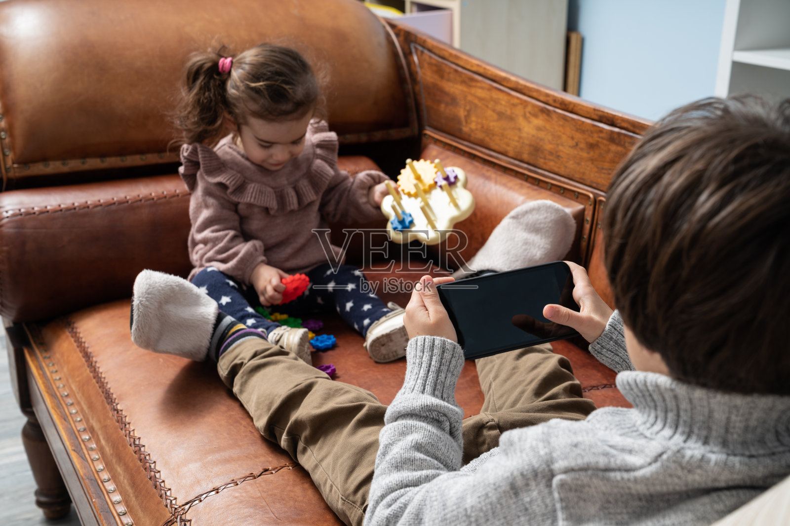 小男孩用智能手机,而他的妹妹在玩玩具照片摄影图片