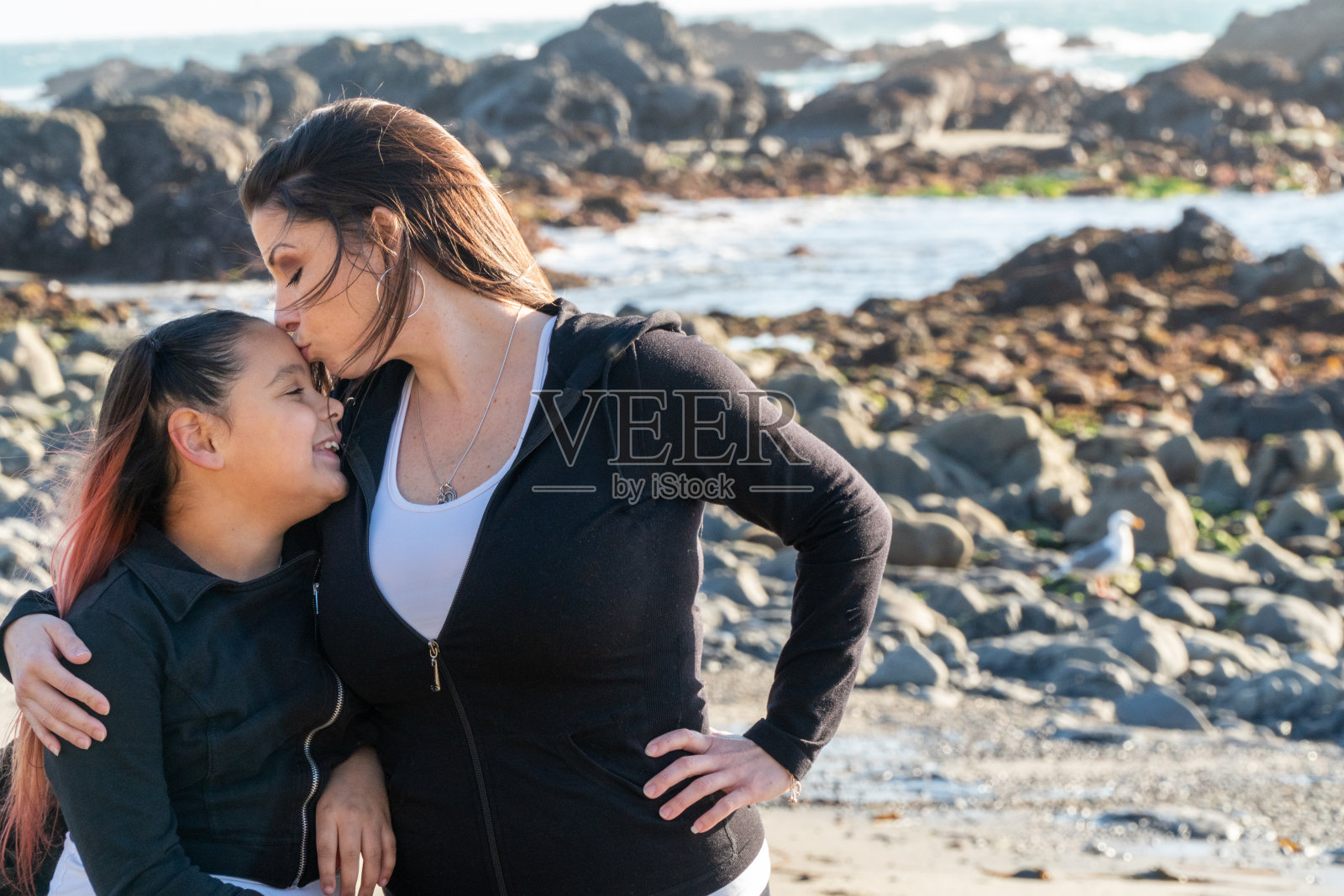 拉丁裔母亲和女儿在海滩拥吻照片摄影图片