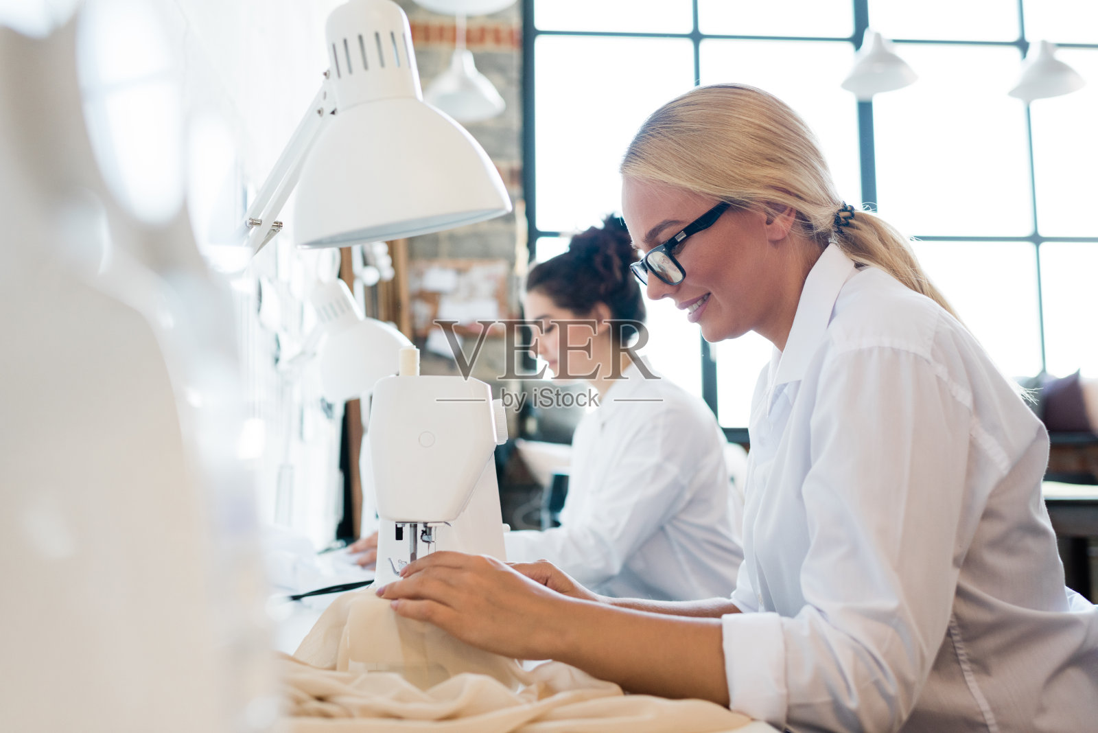女裁缝穿着白衬衫缝制衣服或亚麻布的年轻漂亮的女裁缝照片摄影图片