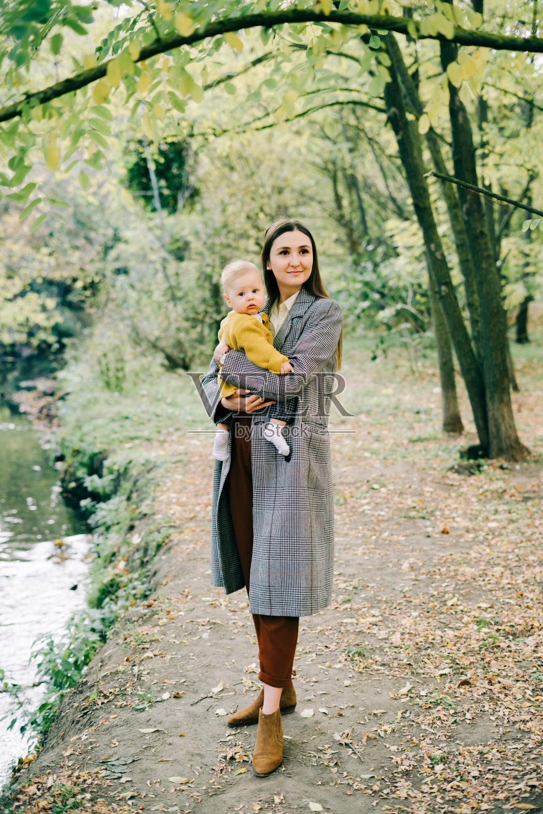 年轻妈妈秋日公园小溪边抱着儿子照片摄影图片