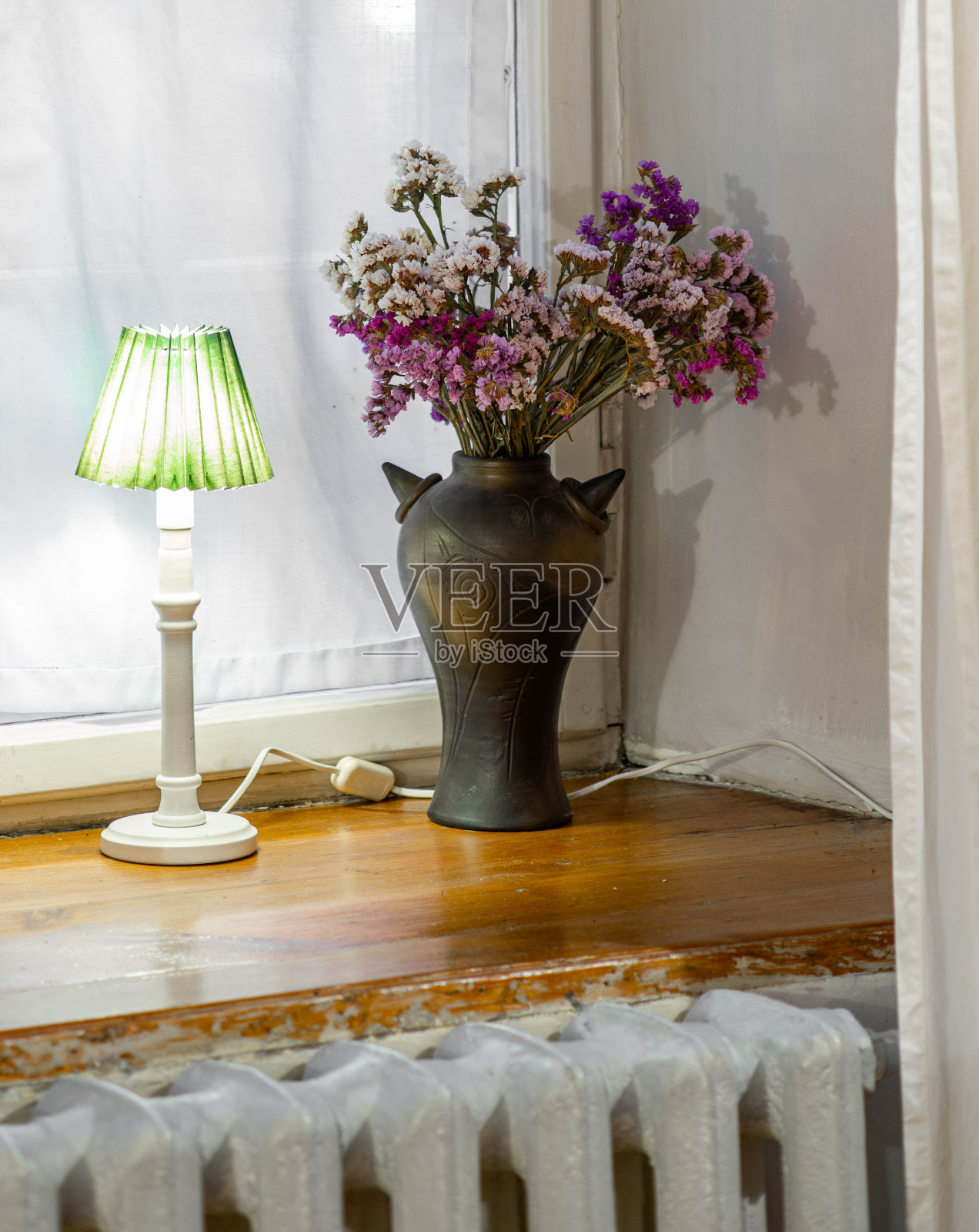 木窗台上放着一盏灯和一个黑色花瓶,上面插着紫色的干花。内部。照片摄影图片