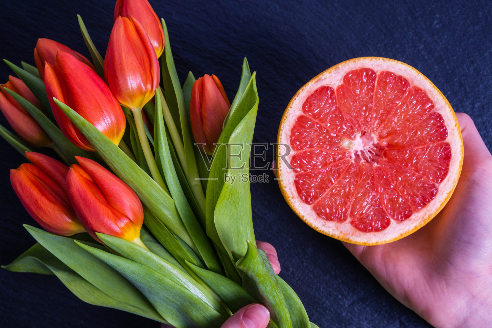 手里拿着橘子,石头上放着一束红色的郁金香照片摄影图片