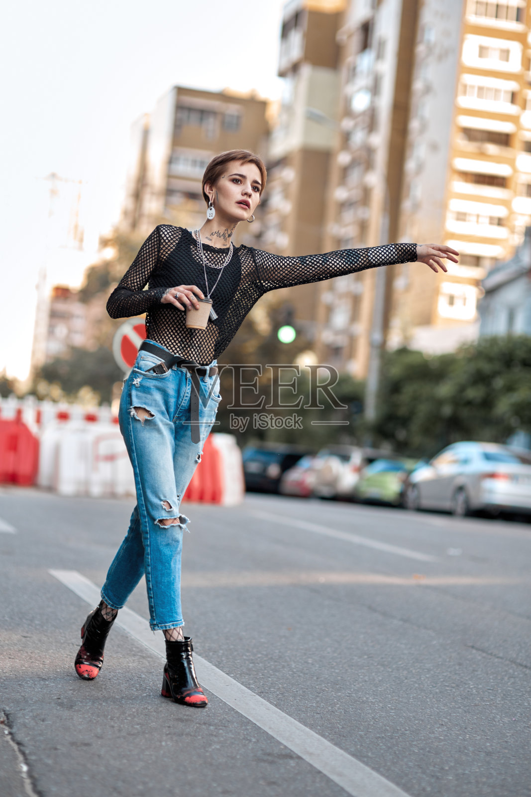 都市风尚:站在户外马路上,手拿咖啡,准备打车的时尚年轻女人照片摄影图片