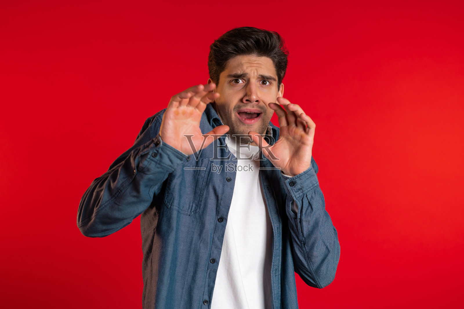 惊恐的欧洲人害怕的东西,看着镜头与大眼睛充满恐惧的红色墙的背景。照片摄影图片