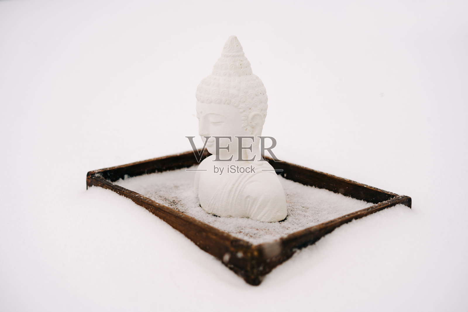 一个用石膏做成的白色小佛像,放在一个冬天下雪时覆盖着白雪的木架上照片摄影图片