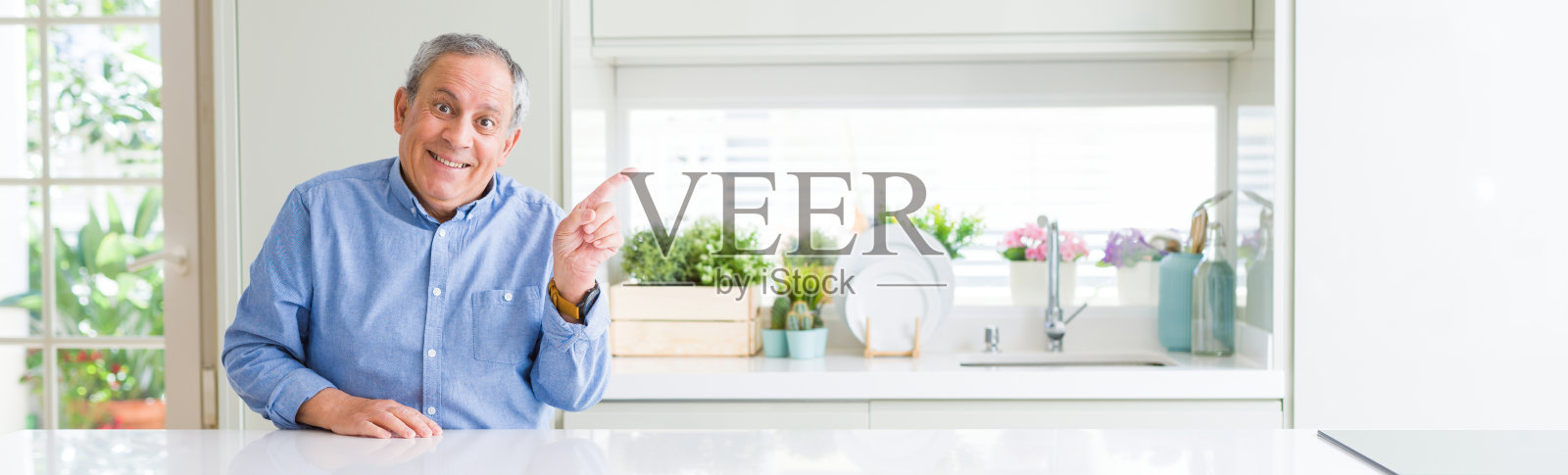 英俊老人居家微笑的广角照片,用手指着侧面看着镜头照片摄影图片