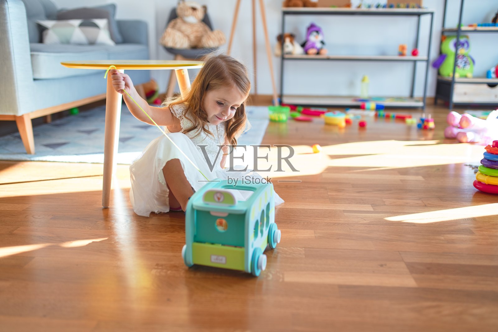 可爱的金发小孩微笑快乐地玩汽车玩具周围的许多玩具在幼儿园照片摄影图片