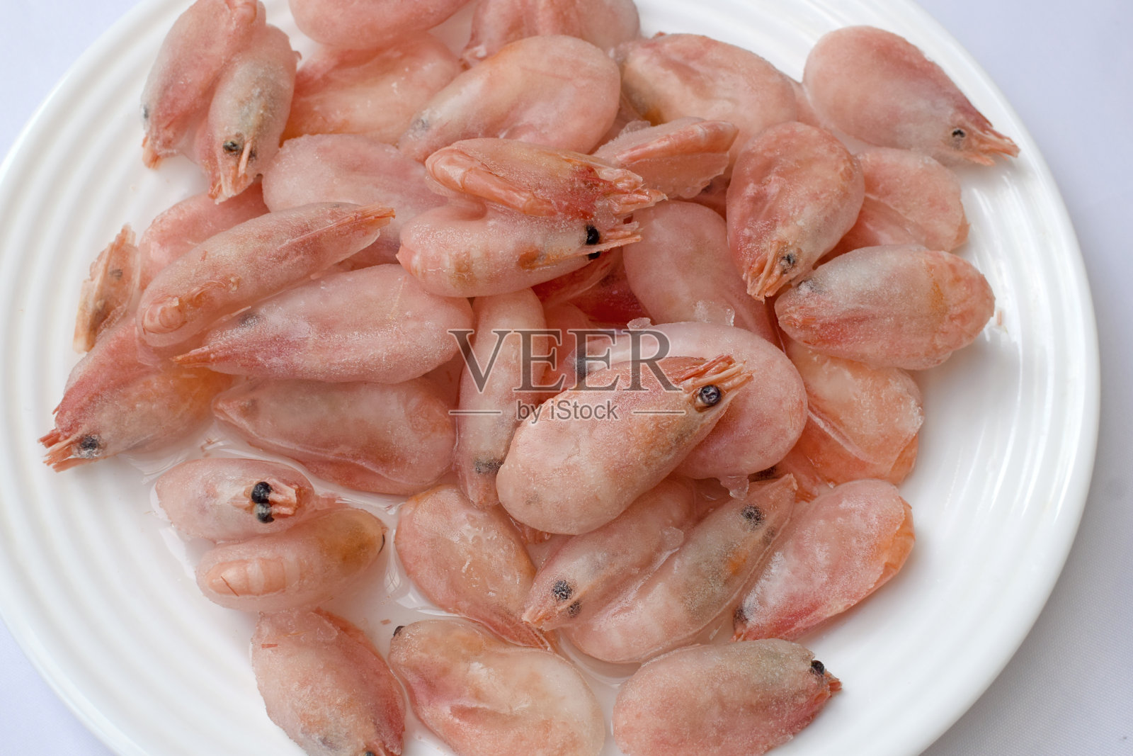 白盘子里放着水煮过的冻虾。照片摄影图片