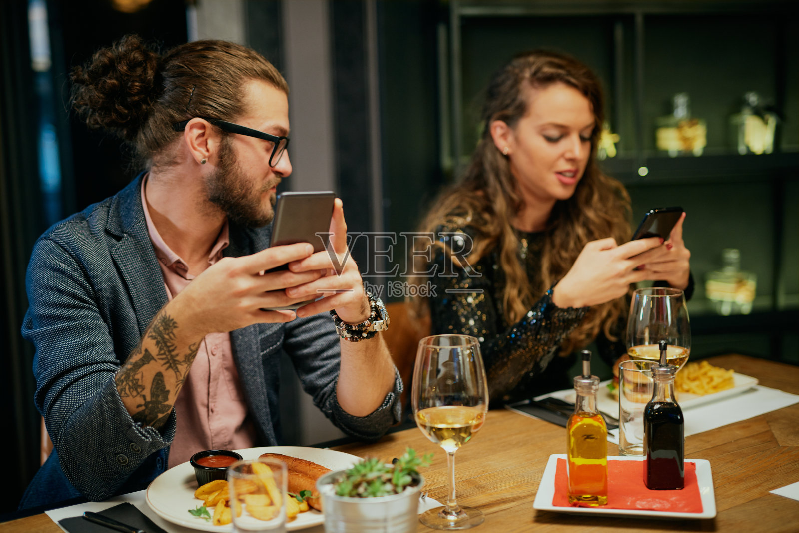 无聊的情侣坐在餐厅里吃晚餐并使用智能手机照片摄影图片