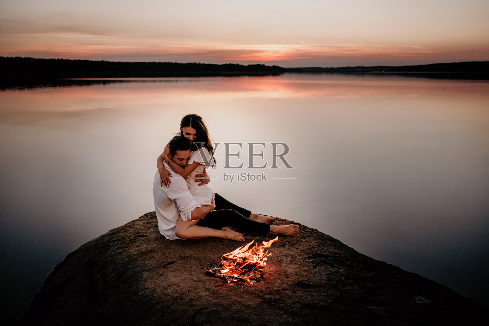 年轻夫妇拥抱和亲吻在日落海岸附近的火。浪漫的爱情故事照片摄影图片