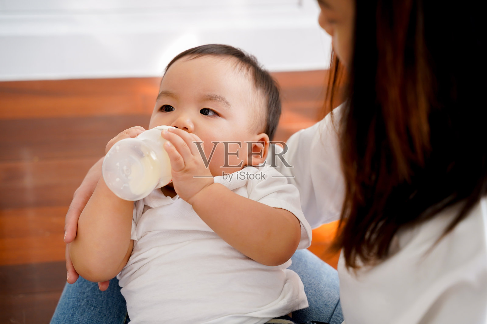 亚洲母亲特写:在客厅里照顾自己的儿子,用奶瓶喂奶——母性和配方奶喂养的新生儿概念照片摄影图片