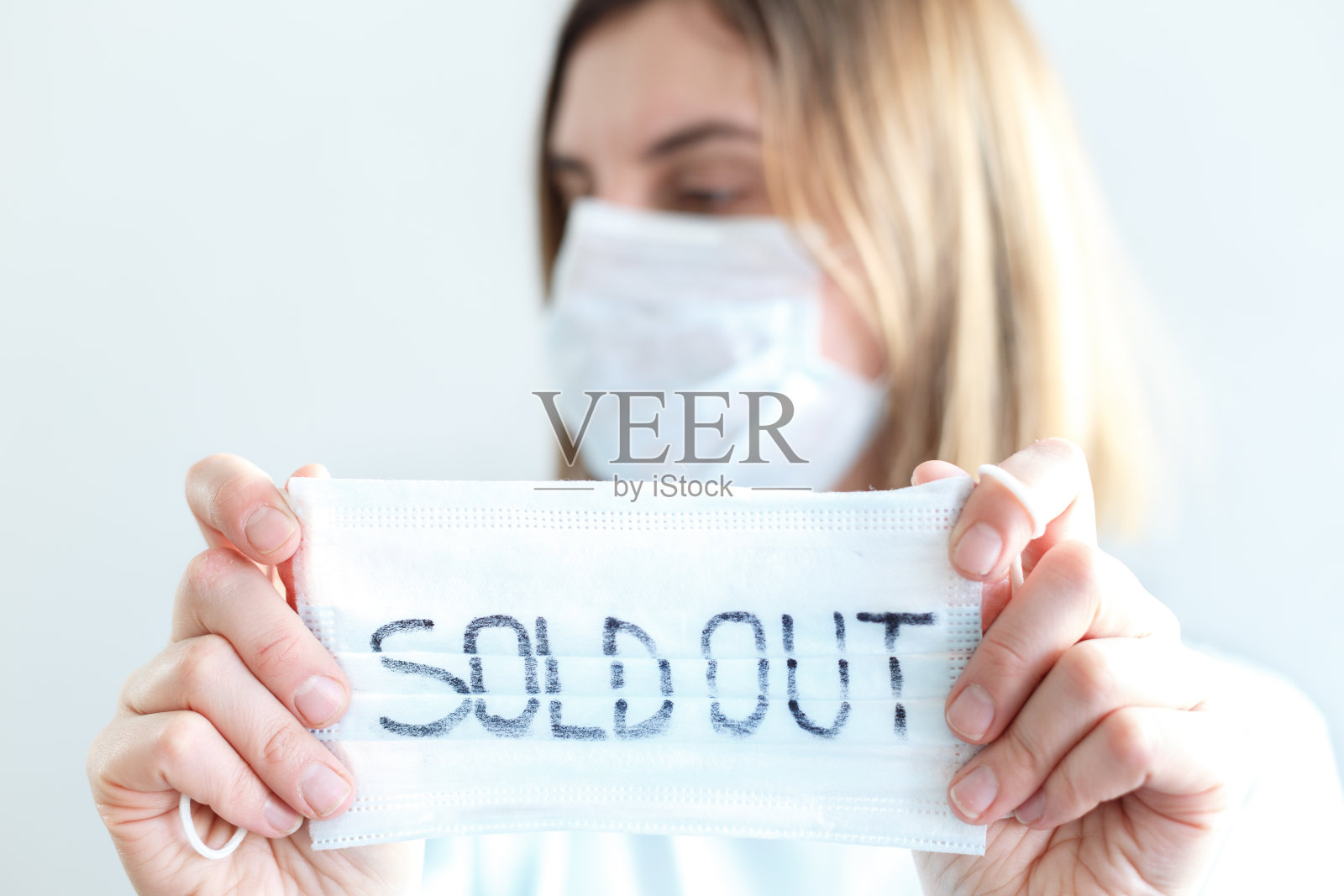 一名身穿一次性蓝色医疗衬衫的妇女手里拿着信息牌,上面写着:口罩脱销,售完。新型冠状病毒(N-CoV)新型流感冠状病毒在发生变异并传播照片摄影图片