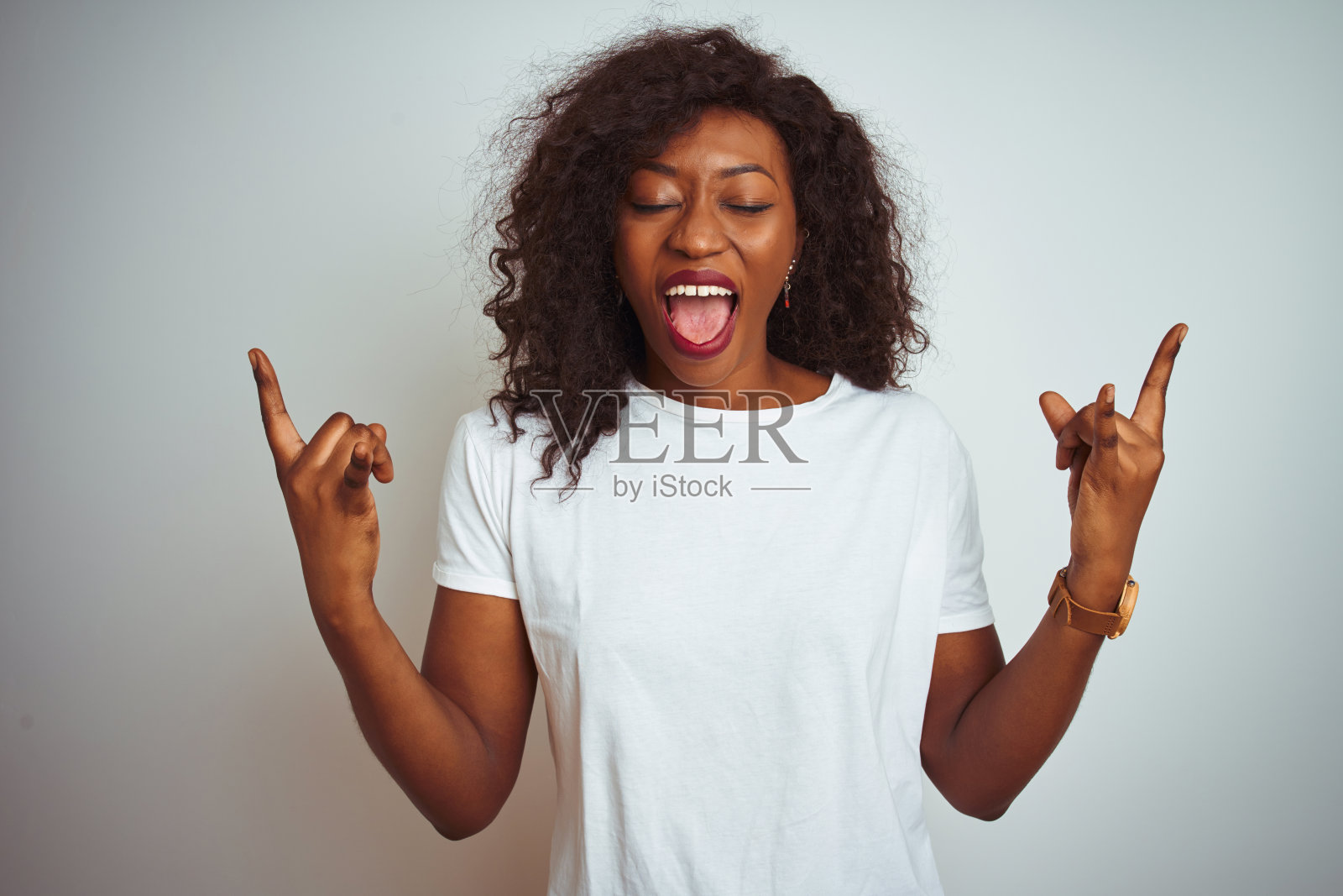 年轻的非洲裔美国妇女穿着t恤站在孤立的白色背景大喊与疯狂的表情做摇滚符号与手举起。音乐明星。沉重的音乐概念。照片摄影图片