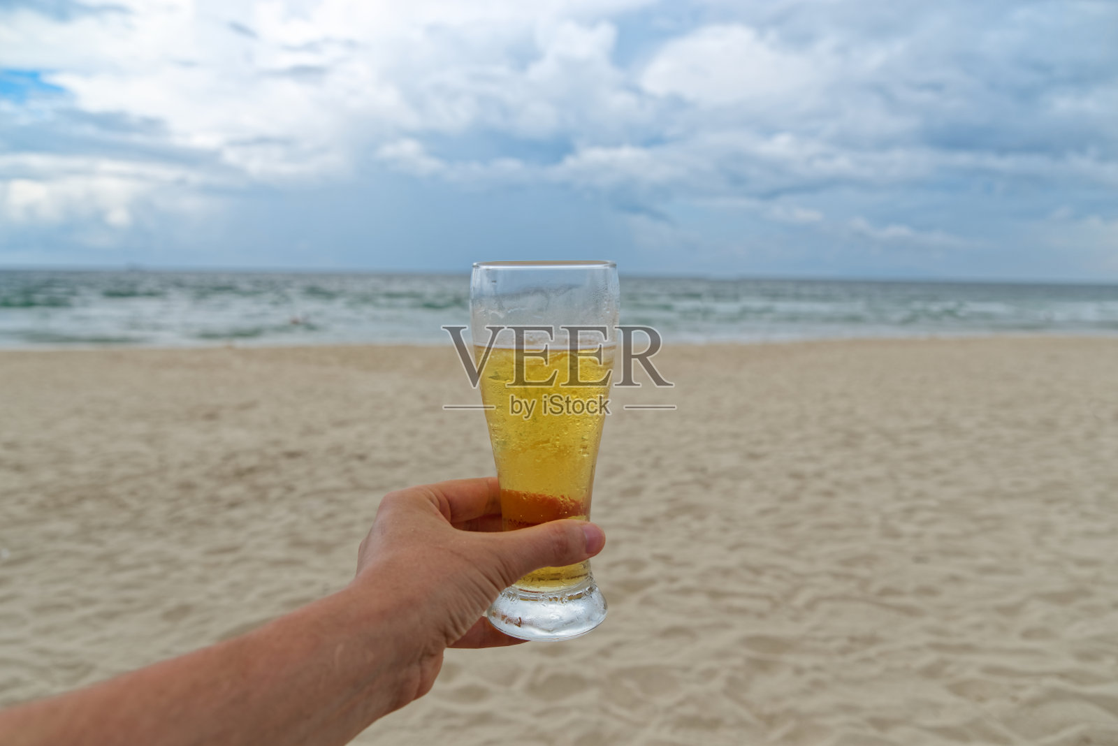 在阴天的沙滩上,男人们手拿着一杯啤酒照片摄影图片