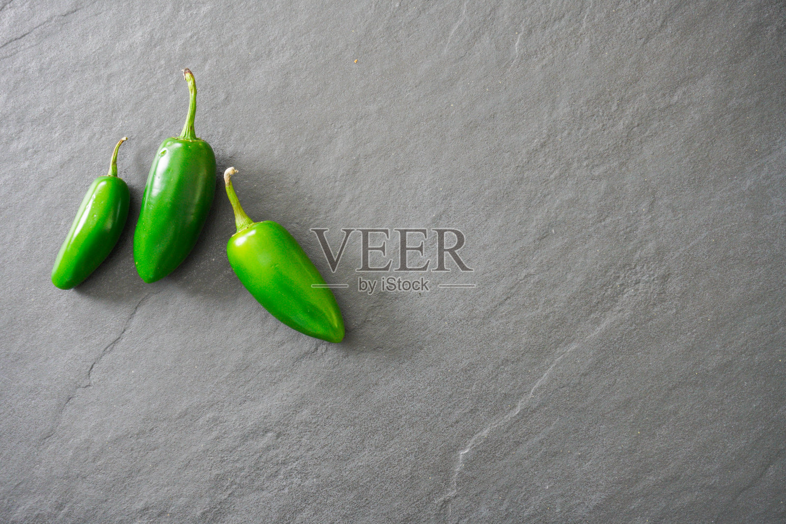 三个鲜绿色的墨西哥辣椒在灰色的石板背景上,有拷贝空间;准备食物照片摄影图片