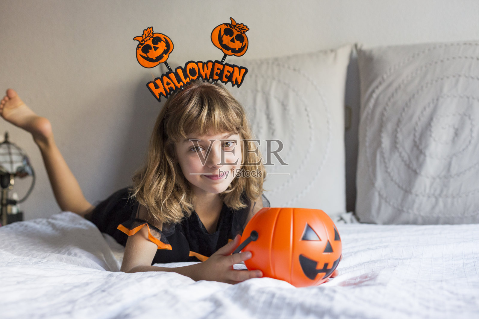 美丽的小女孩微笑着,穿着万圣节的服装在床上。玩南瓜。家,在室内,生活方式照片摄影图片