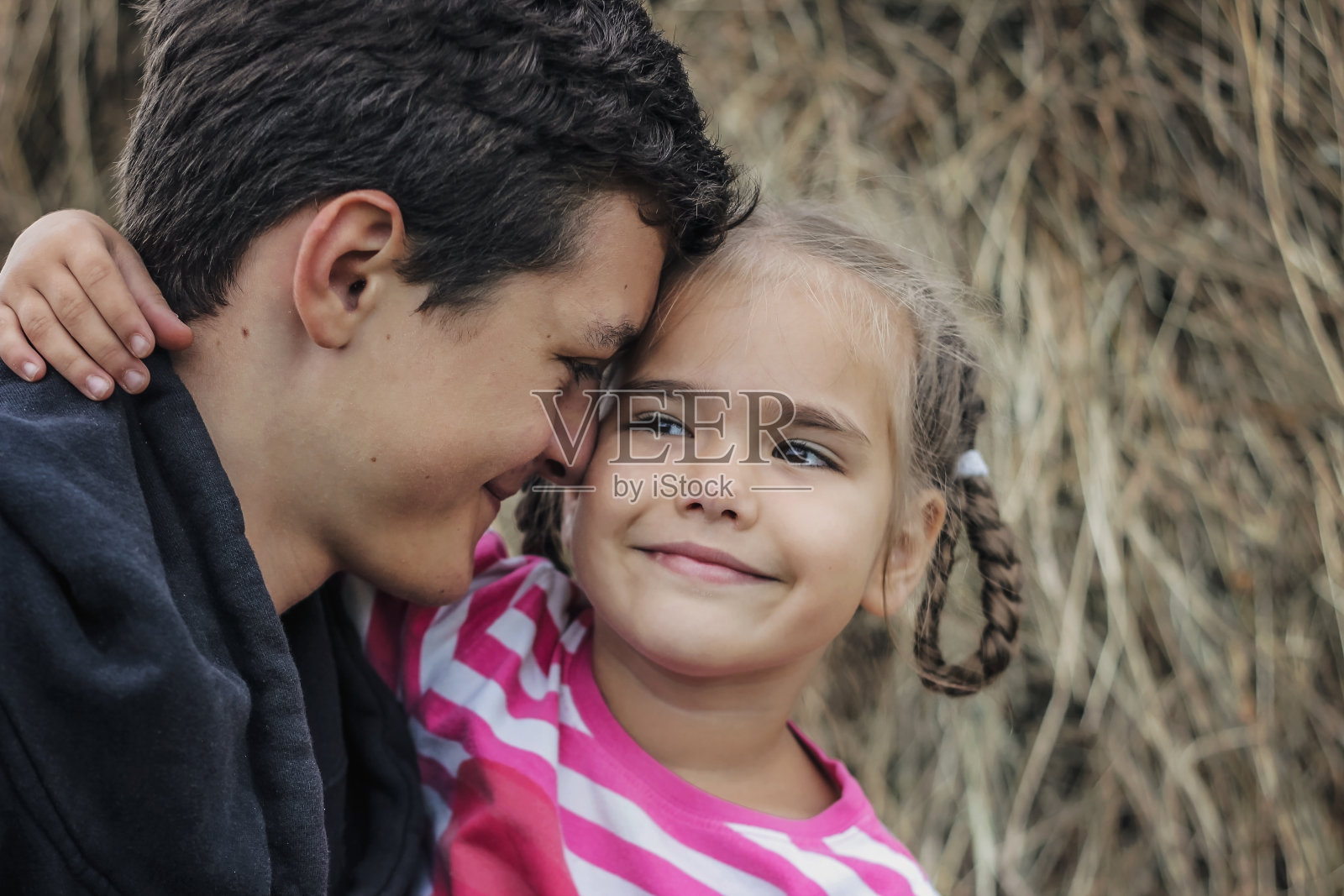 在草地上夏季散步时拥抱她可爱的妹妹的少年照片摄影图片