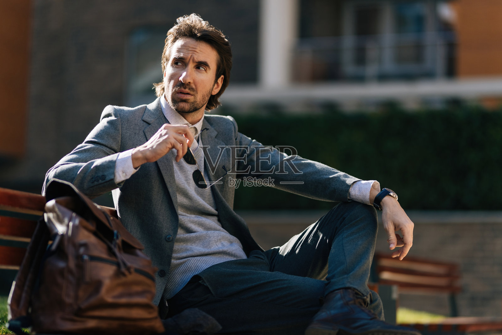 年轻沉思的商人在城市的长椅上休息。照片摄影图片