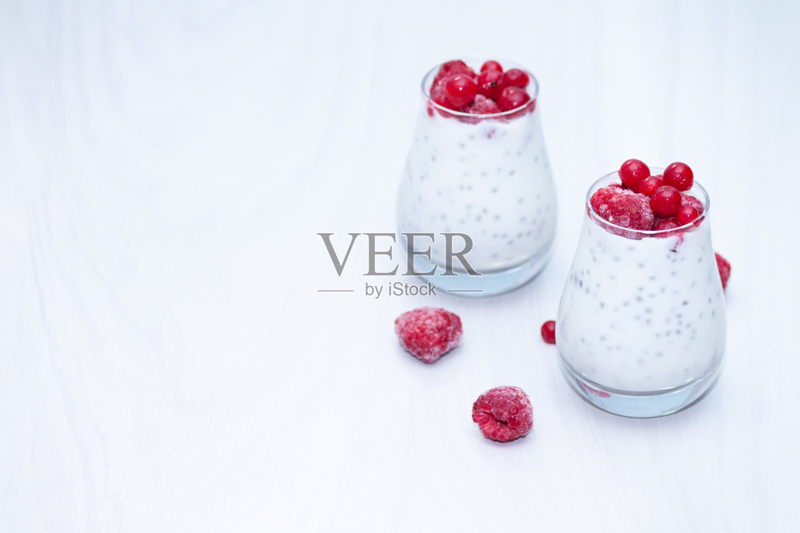 健康的香草奇亚布丁与红色的浆果在白色的木制背景。健康的零食的概念。副本的空间。照片摄影图片